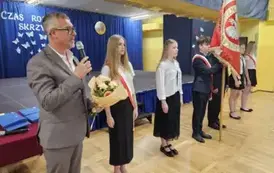 Przem&oacute;wienie naczelnika wydziału edukacji na tle pocztu sztandarowego szkoły