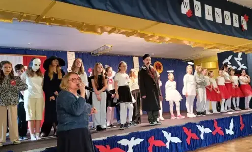 Pani dyrektor na tle uczniów i sceny przemawia do zgromadzonych